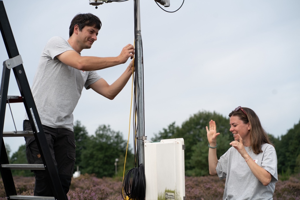 two scientists around a measurement tower with a field in the background