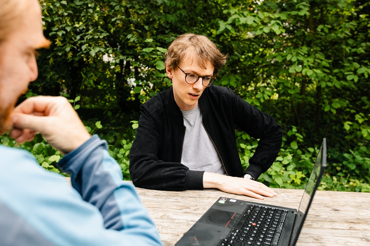 Research technician Achim Holtman sitting outside looking at a laptop with a colleague