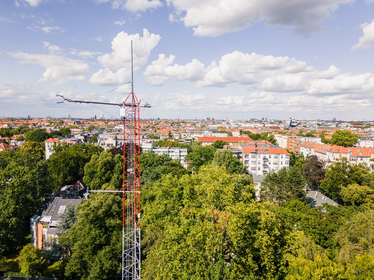 Picture of the measurement tower reaching over the trees with a city landscape on the background