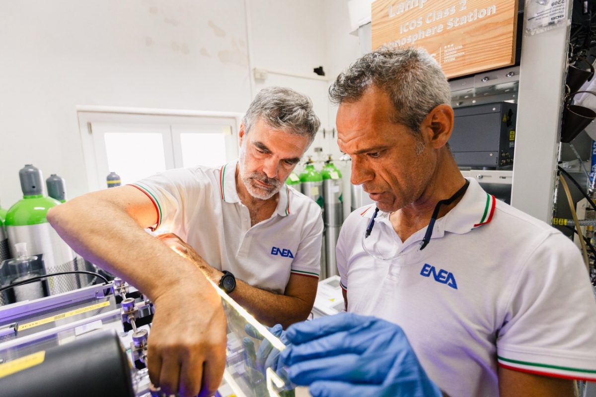 wo ENEA researchers examine scientific equipment inside a laboratory, with gas cylinders and instrumentation visible in the background.