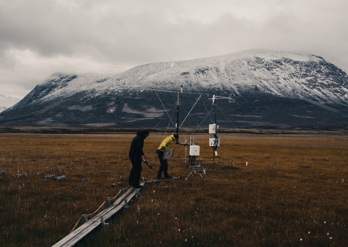 Scienziati al lavoro attorno a una torre di misurazione con una montagna innevata sullo sfondo.