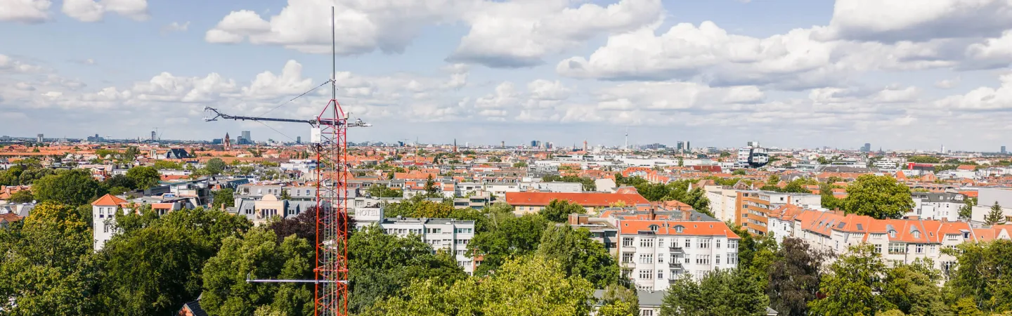 Atmospheric measurement tower above treetops with a city skyline in the background
