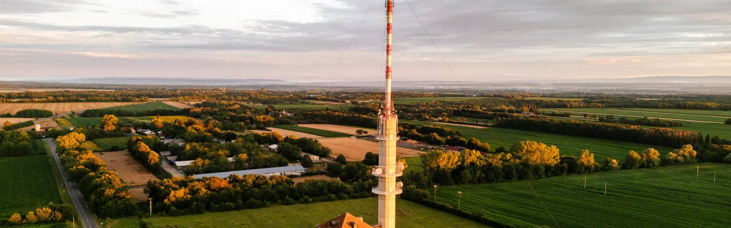 Tall measurement tower beside a small building, surrounded by farmland at sunset
