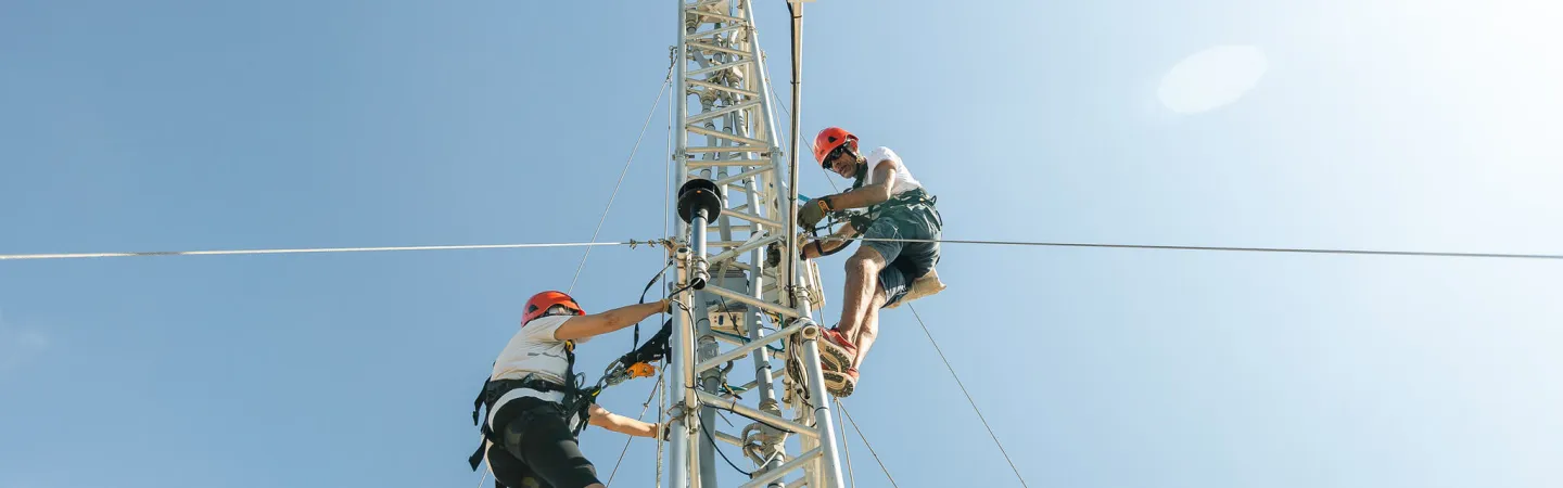 Technicians climbing an atmospheric measurement tower against a clear sky