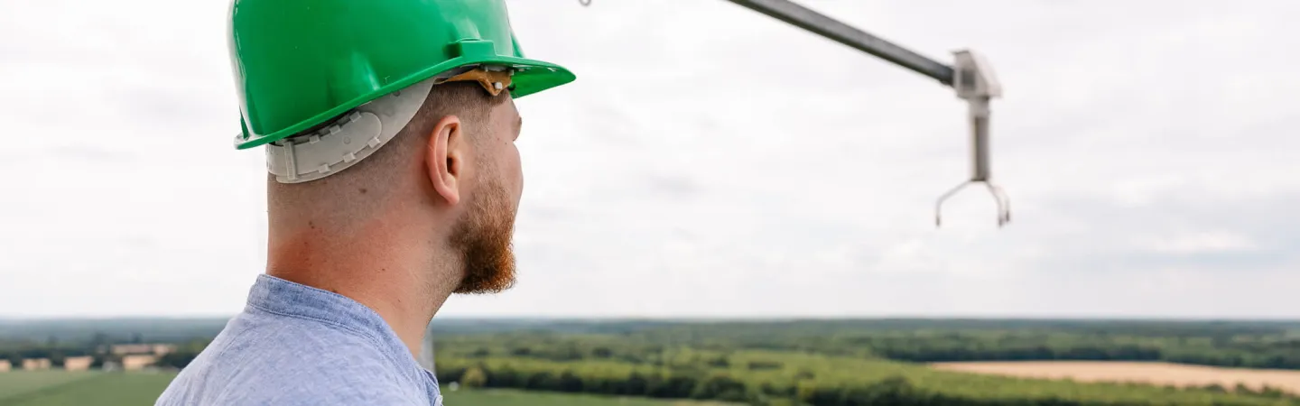 Man wearing a green hard hat overlooking farmland from a raised platform.