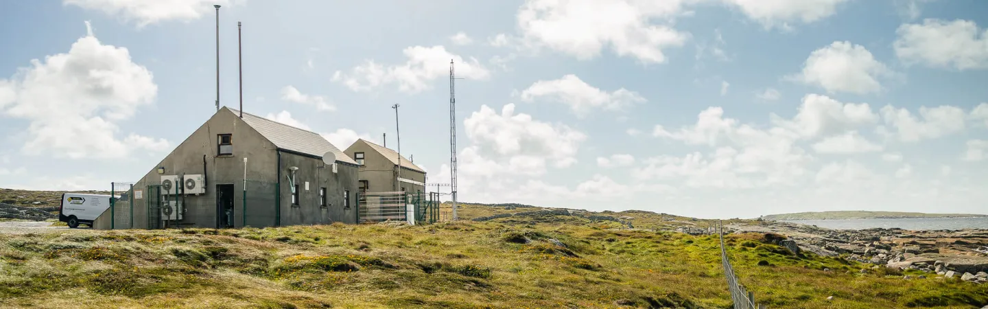 Small research building with antennas in a grassy coastal landscape