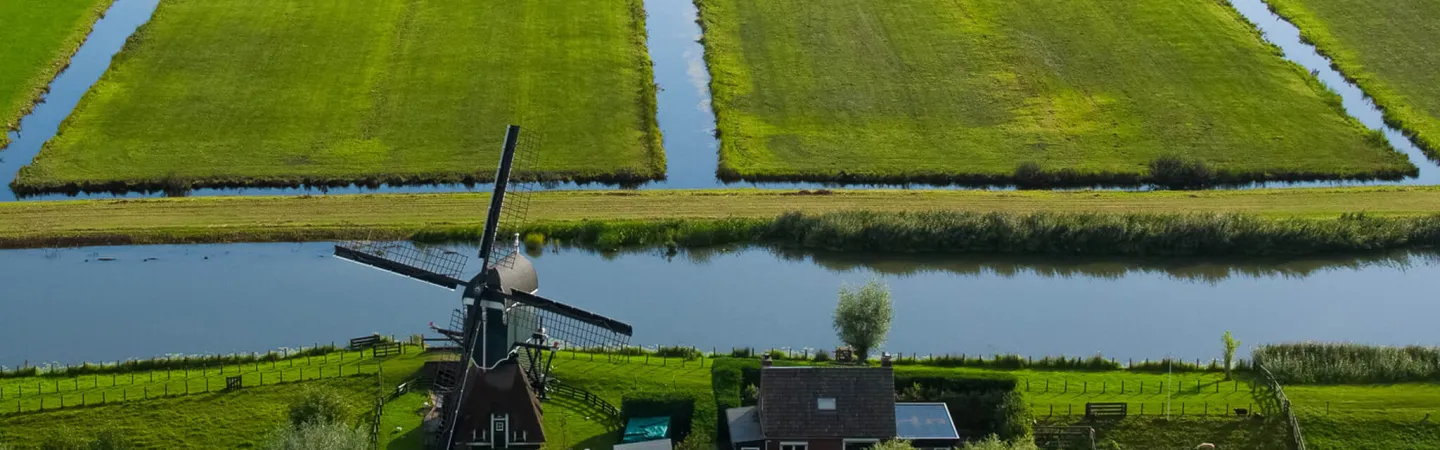 Traditional windmill and house beside canals and green fields