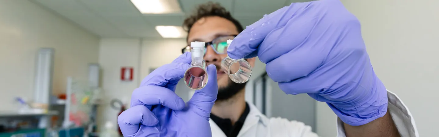 Scientist in a laboratory holding two small glass vials with liquid samples