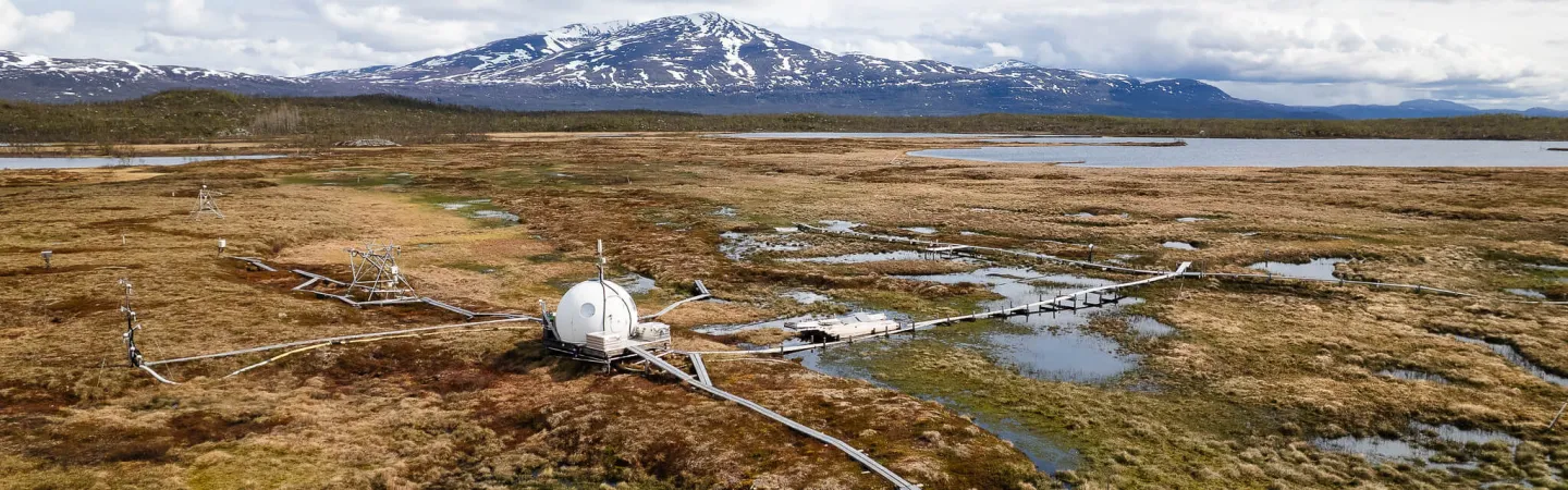 Wetland research site with boardwalks and instruments beneath snow-capped mountains
