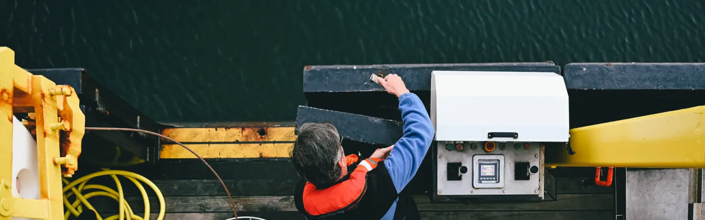 Researcher operating equipment on a boat deck above dark water.
