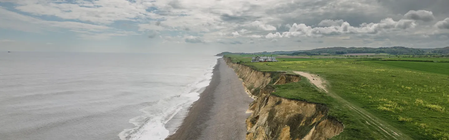 Eroding coastal cliffs with farmland and houses above the shoreline.