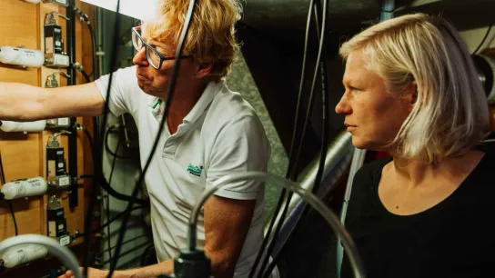 Two people standing next to each other are looking to the left at measuring instruments.