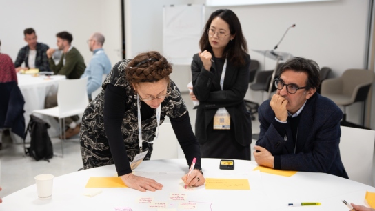three people around a table writing on colourful post it notes 