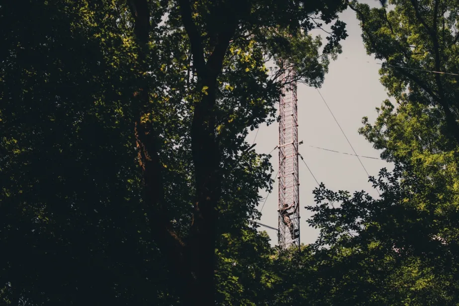 man climbing up a measurement tower in a green forest